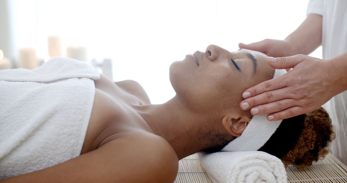 Professional massage therapist massaging female face at beauty salon.